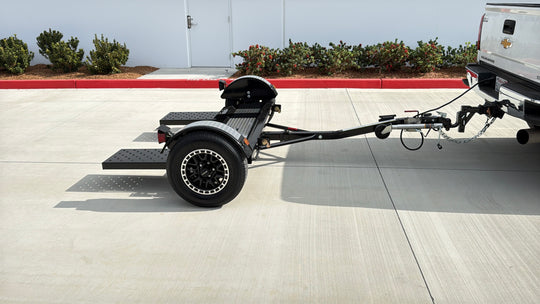 Side view of Premier car tow dolly showing 2 inch ball coupler, safety chains, and wiring harness connected to truck