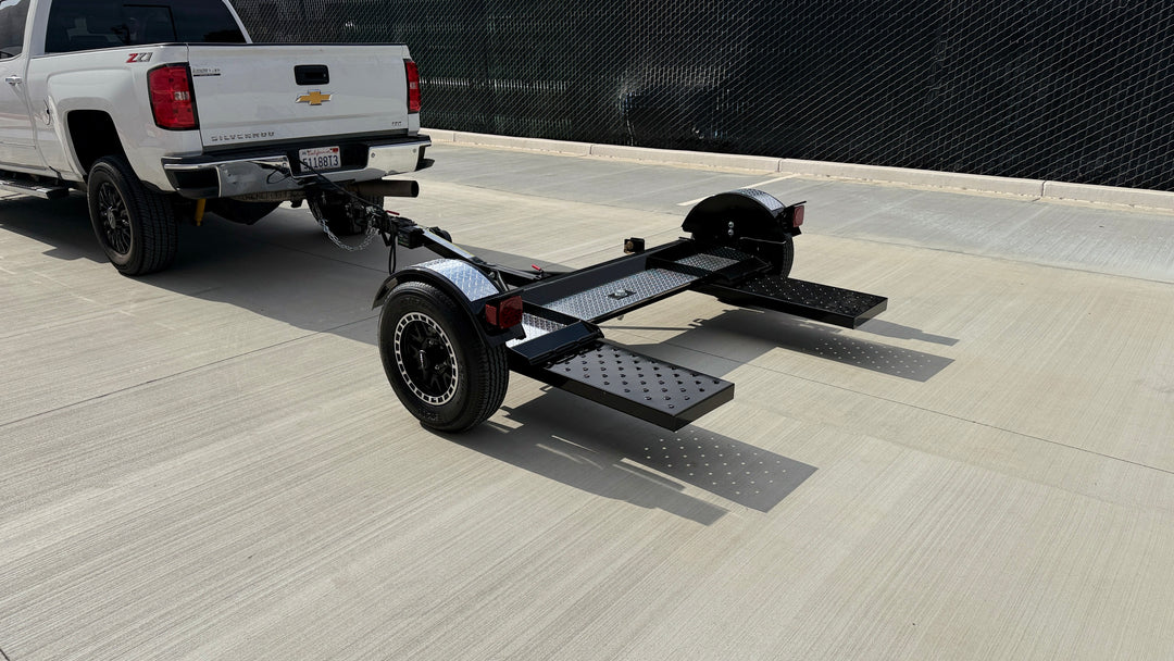 Black and chrome car tow dolly with ramps extended, three-quarter rear view, hitched and ready to tow