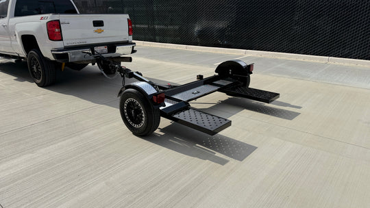 Black and chrome car tow dolly with ramps extended, three-quarter rear view, hitched and ready to tow